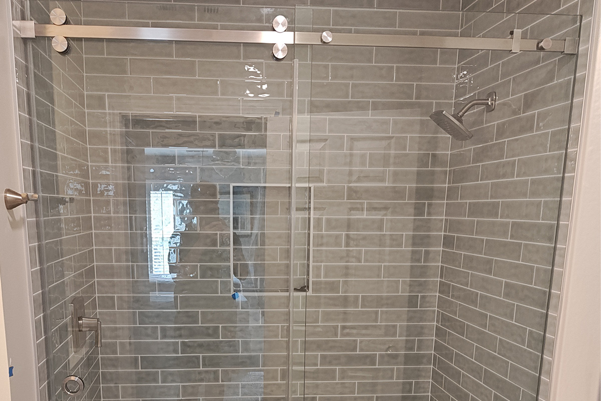 Frameless shower doors in Atlanta with sliding door and metal hardware, gray subway-tiled walls, and a ceiling-mounted rainfall shower head.