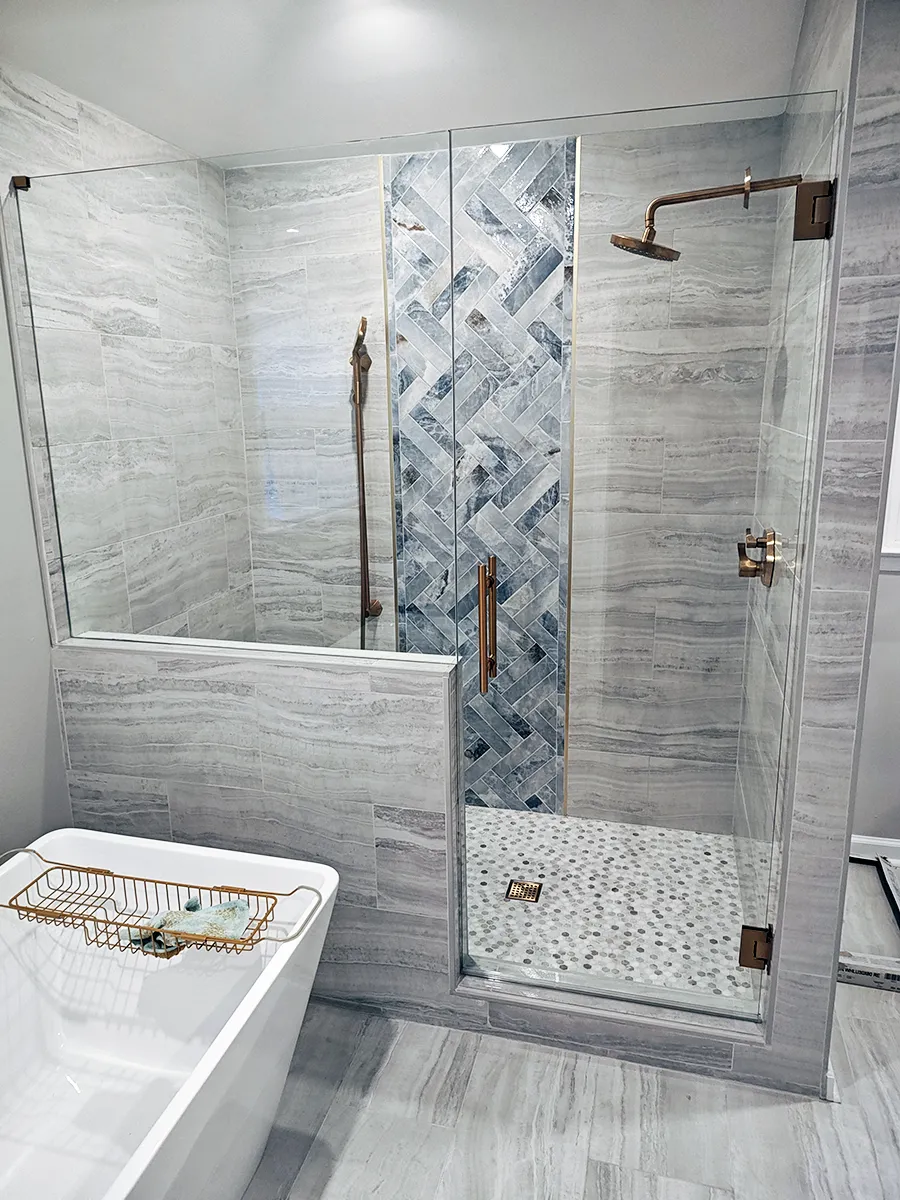 Frameless shower door with brushed gold hardware and gray tile installed in a Roswell, GA bathroom