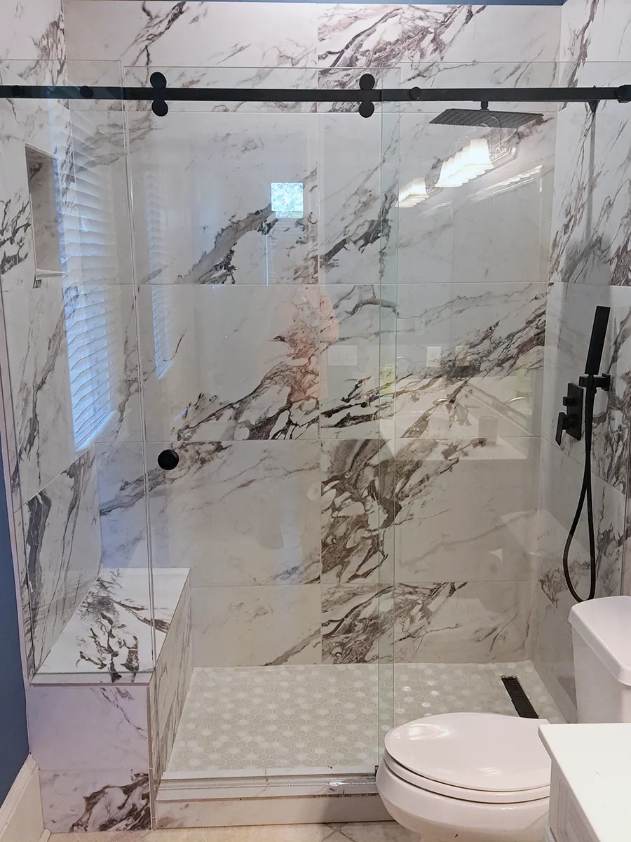 Custom frameless sliding shower enclosure with added seat panel and matte black hardware in Woodstock, GA.