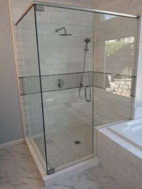 90-degree frameless corner shower with a brushed nickel top support header, clear glass, white subway tile, mosaic accents, and a rain shower.