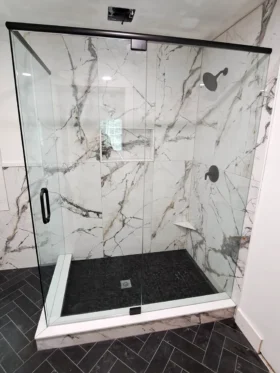 90-degree frameless shower door with matte black top header, return panel, and dark pebble shower floor in Kennesaw, GA.