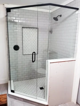 Neo-angle frameless shower with a matte black support header, tiled half wall, clear glass, white subway tile, recessed niche, and white mosaic floor.