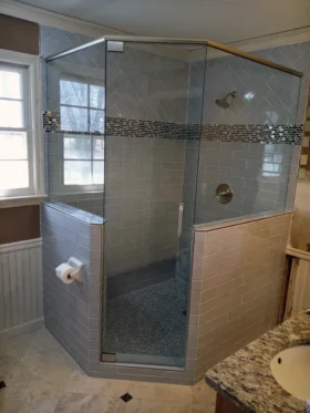 Neo-angle frameless shower with brushed nickel hardware, a top support header, tiled half walls, clear glass, gray subway tile, and mosaic accents.