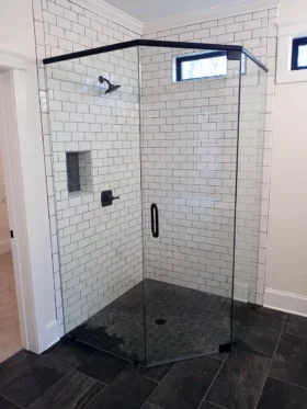 Neo-angle frameless shower with a matte black support header and hardware, clear glass, white subway tile, recessed niche, and dark mosaic floor.